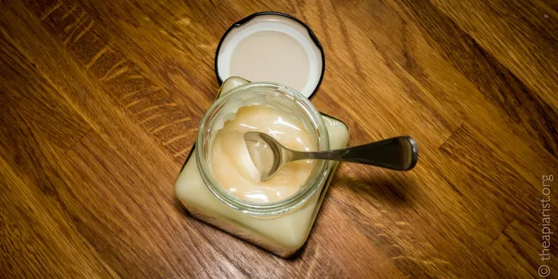 An open jar of honey with a teaspoon in it, sitting on a wooden tabletop