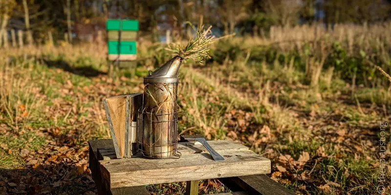 A beekeeper's smoker sitting on a wooden plank in a field.